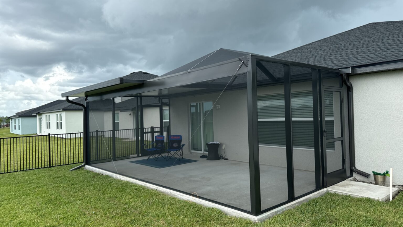 A modern screen room attached to a Florida home, offering a spacious bug-free outdoor area perfect for relaxing—even under cloudy skies.